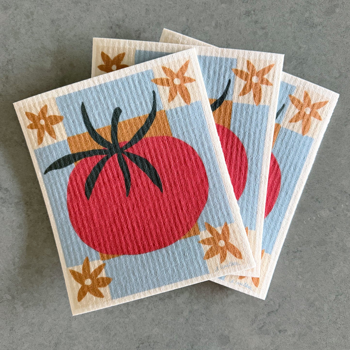 Three square dishcloths with a retro tomato design, stacked on a textured gray surface.
